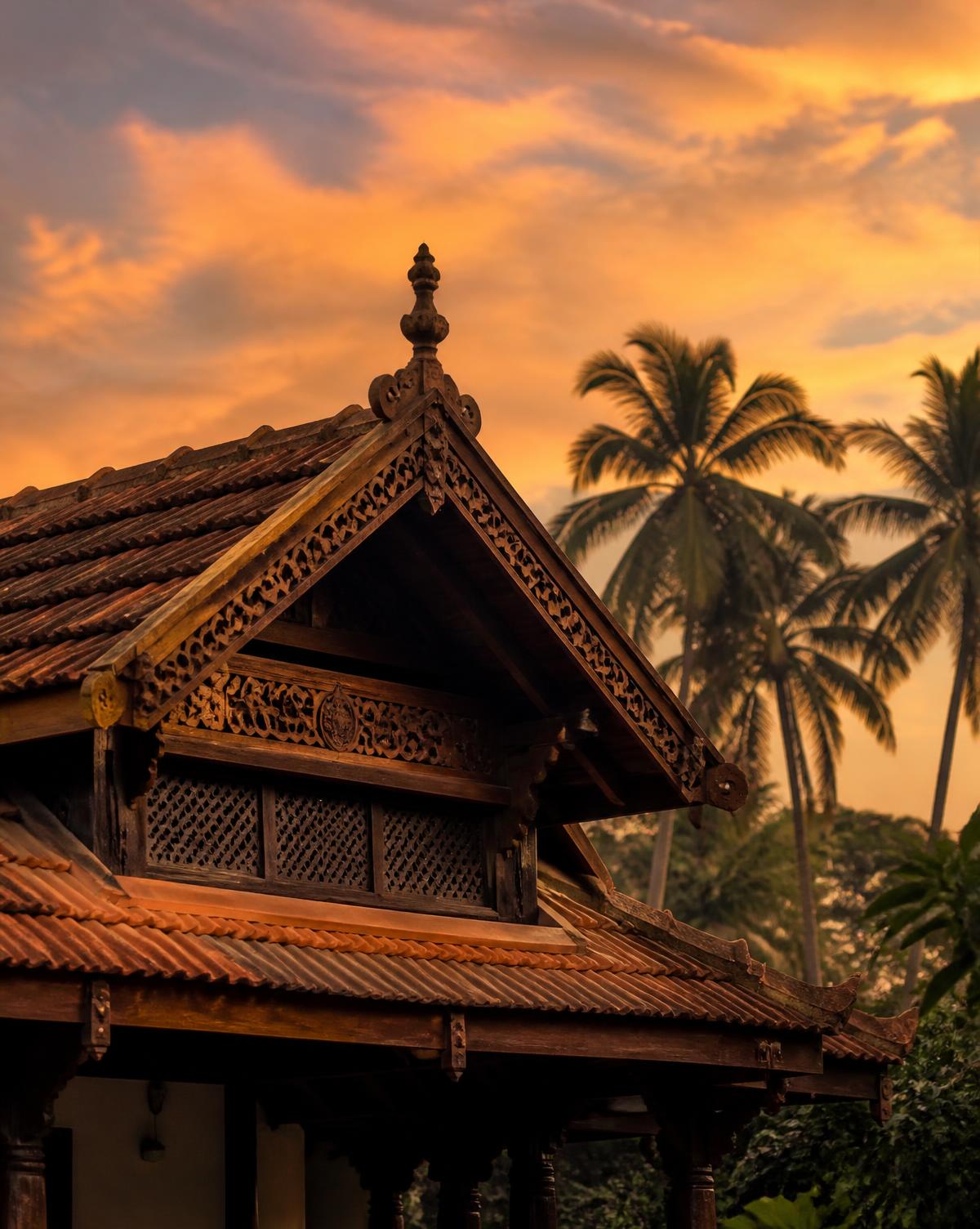 Carved teak gable and terracotta tiled roof of a traditional Kerala villa at sunset